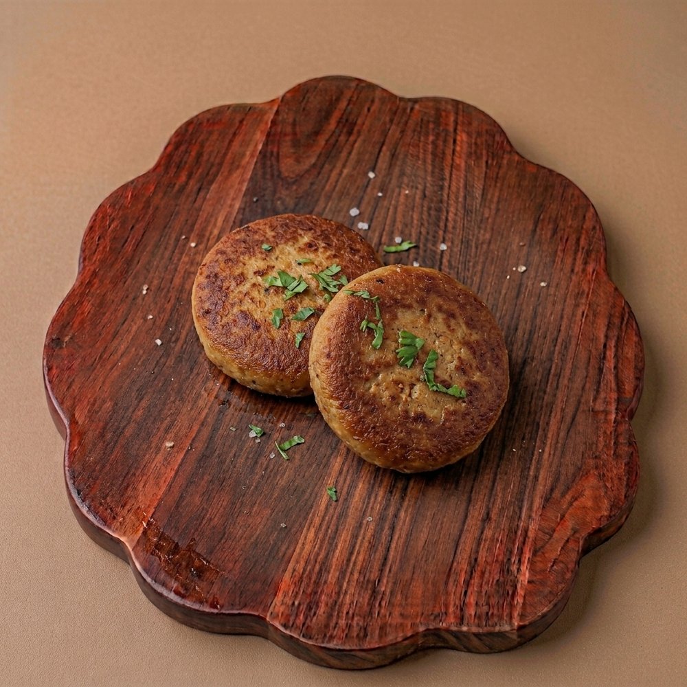 Two cooked chicken shami kebabs topped with fresh coriander on a wooden serving board