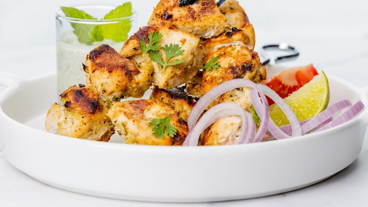 Grilled chicken tikka pieces in a white dish with mint raita, red onion and lime