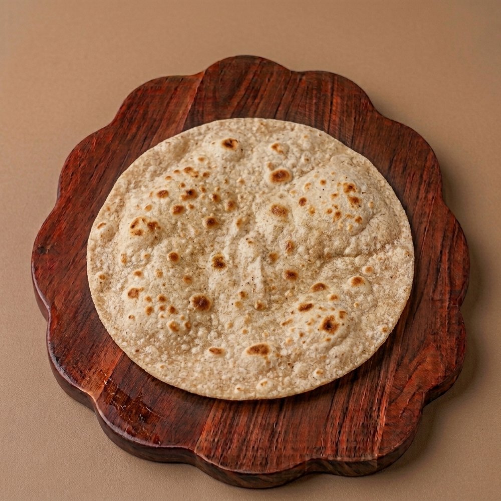 A whole wheat roti with a blistered surface on a wooden serving board